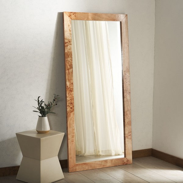 Wooden floor mirror with a white vase and plant on a small table against a plain wall.
