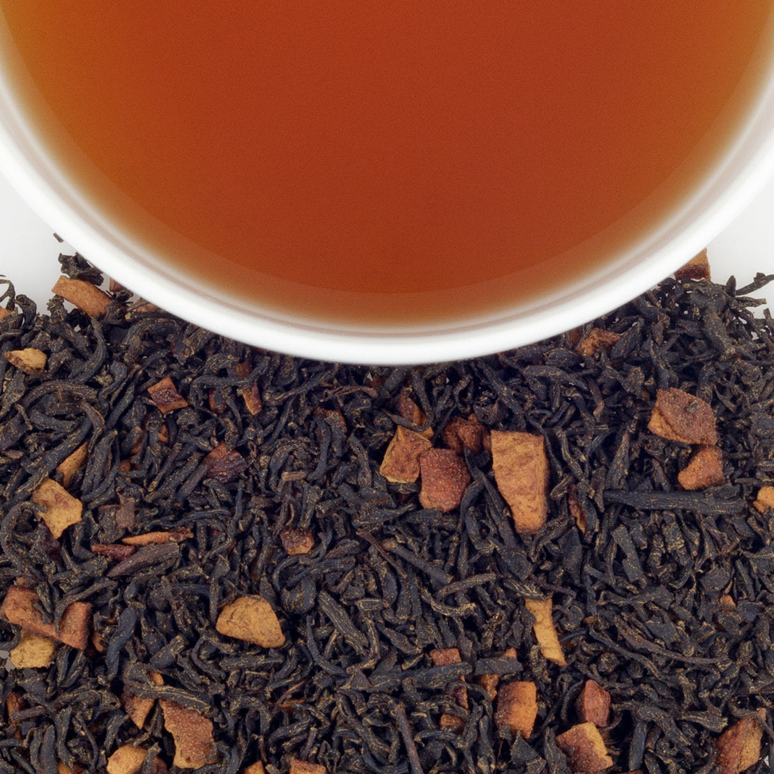Close-up of black tea leaves with a cup of tea in the background