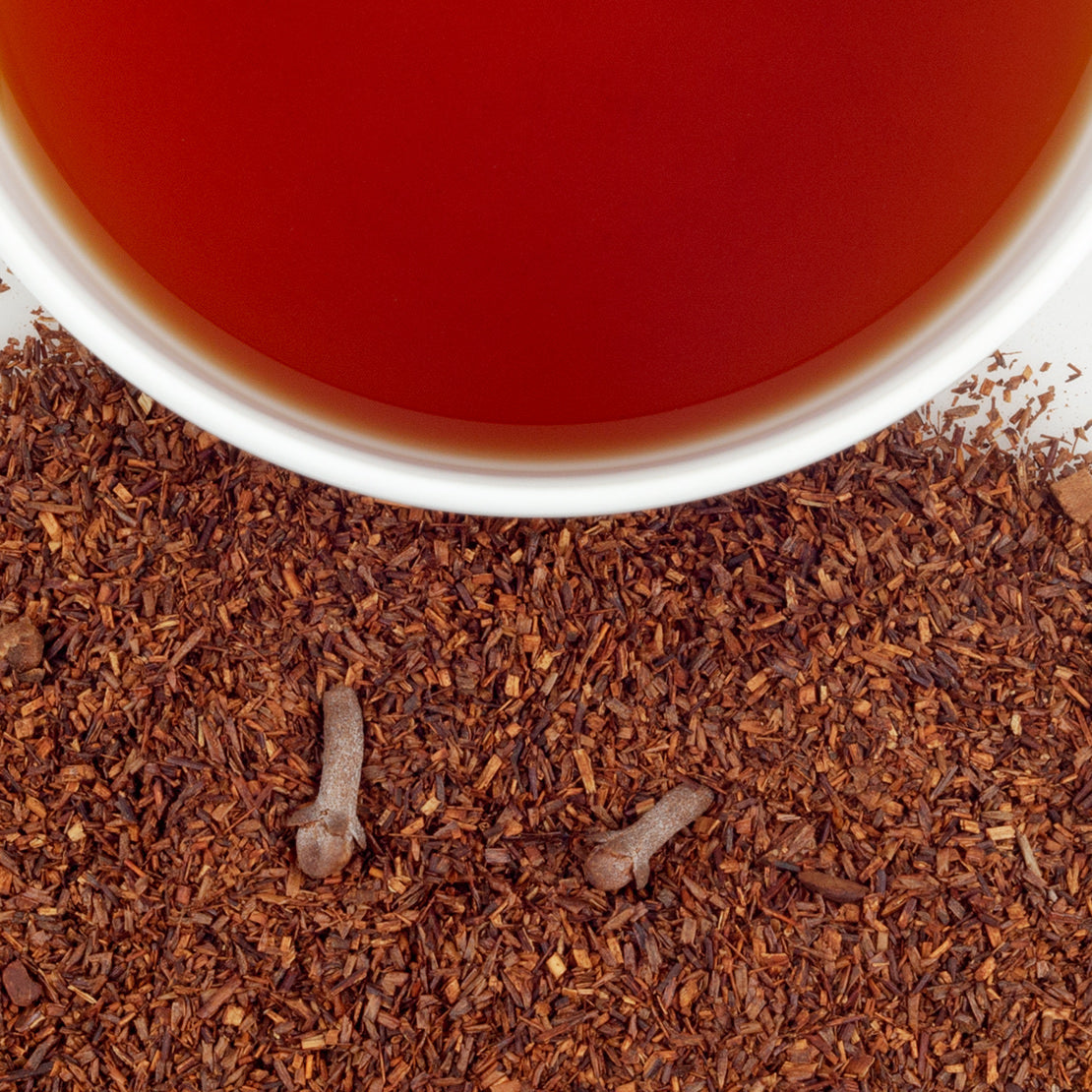 Close-up of a cup of red tea with scattered tea leaves on a white surface