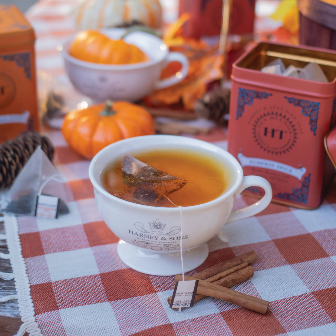 Tea cup with Harney & Sons tea bag on a checkered tablecloth with pumpkins and tea boxes in the background.