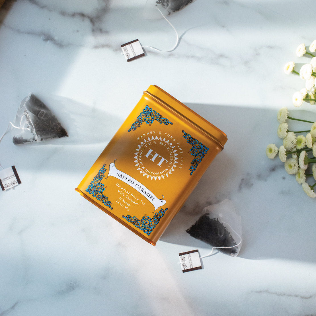 Orange tea box with 'HT' branding on a marble surface with tea bags and flowers.
